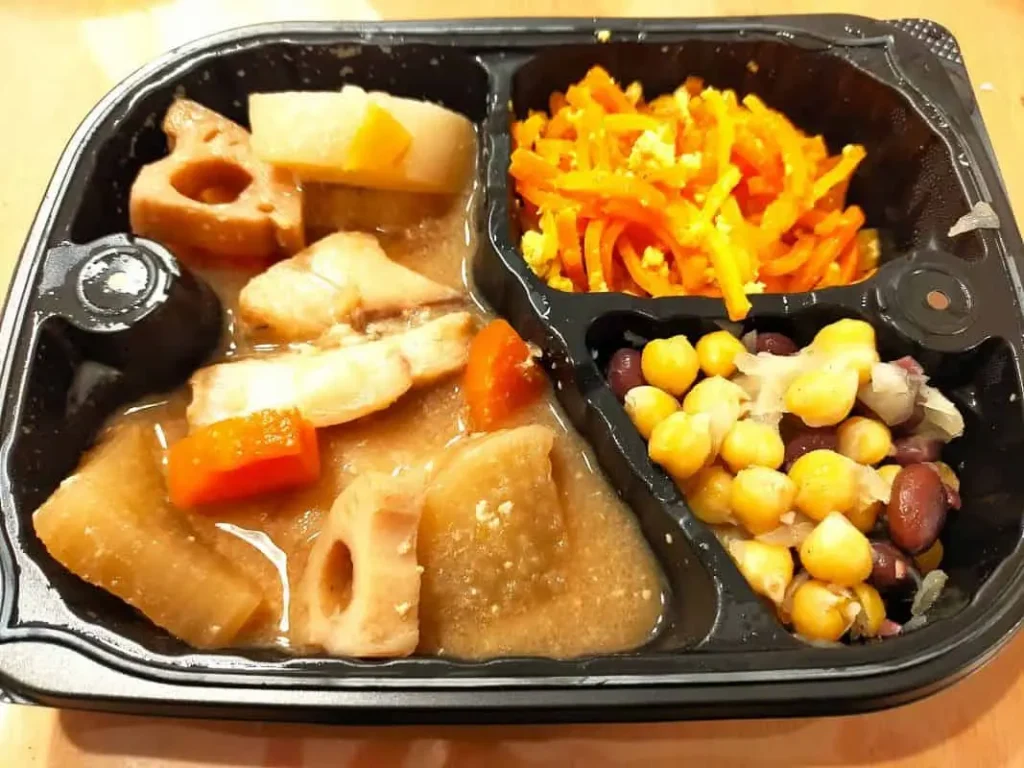 わんまいるの美食弁当。主菜は三陸産さくらますと根菜の味噌煮で、大根、れんこん、にんじんなどがごろごろと入っている。副菜には人参しりしりと豆のマリネが添えられている。