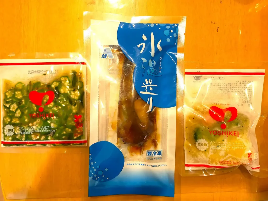ヨシケイの冷凍宅配食材3品。オクラ、魚の切り身、洋風の野菜料理がそれぞれ個包装されて並んでいる。