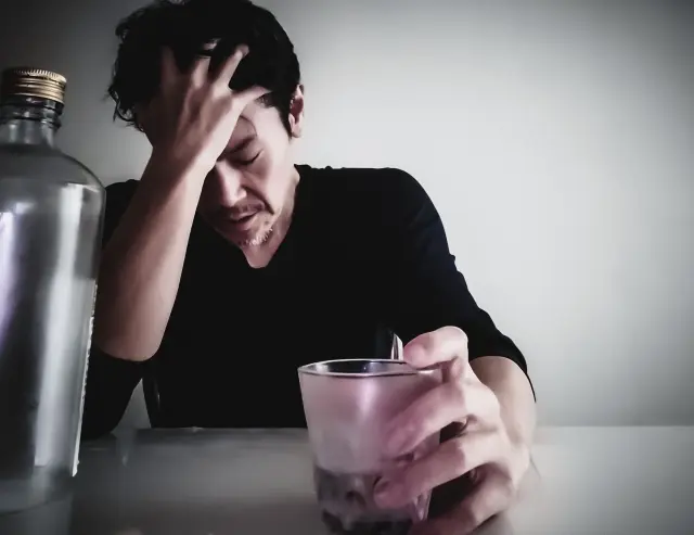 お酒を飲みすぎて体調がすぐれず頭を抱えている男性