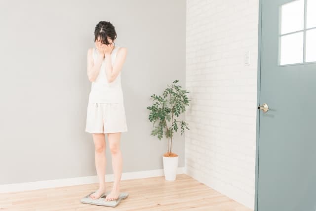 体重計に乗っている女性が顔を覆っている画像